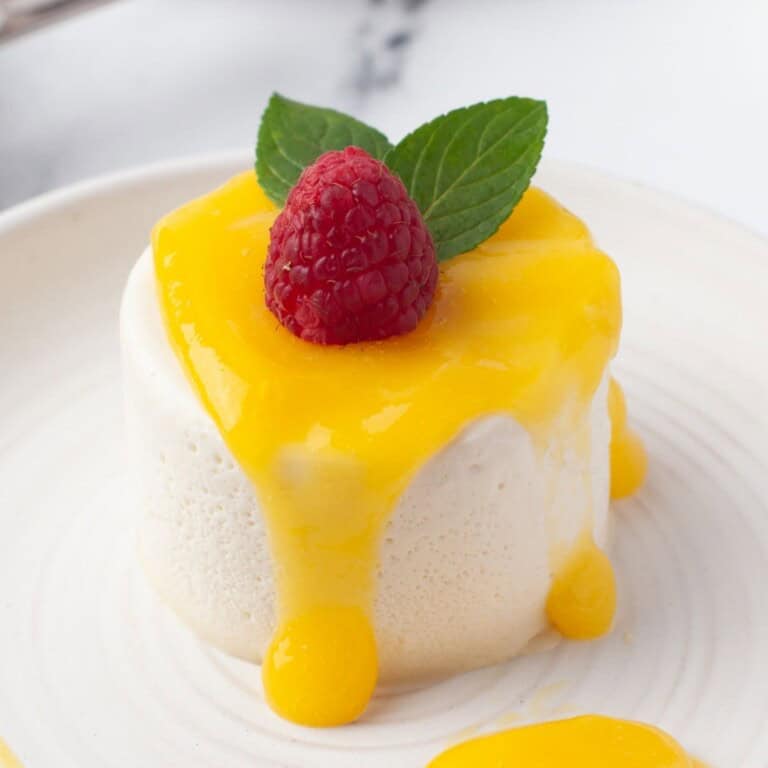 panna cotta with mango sauce and garnished with a raspberry and two mint leaves