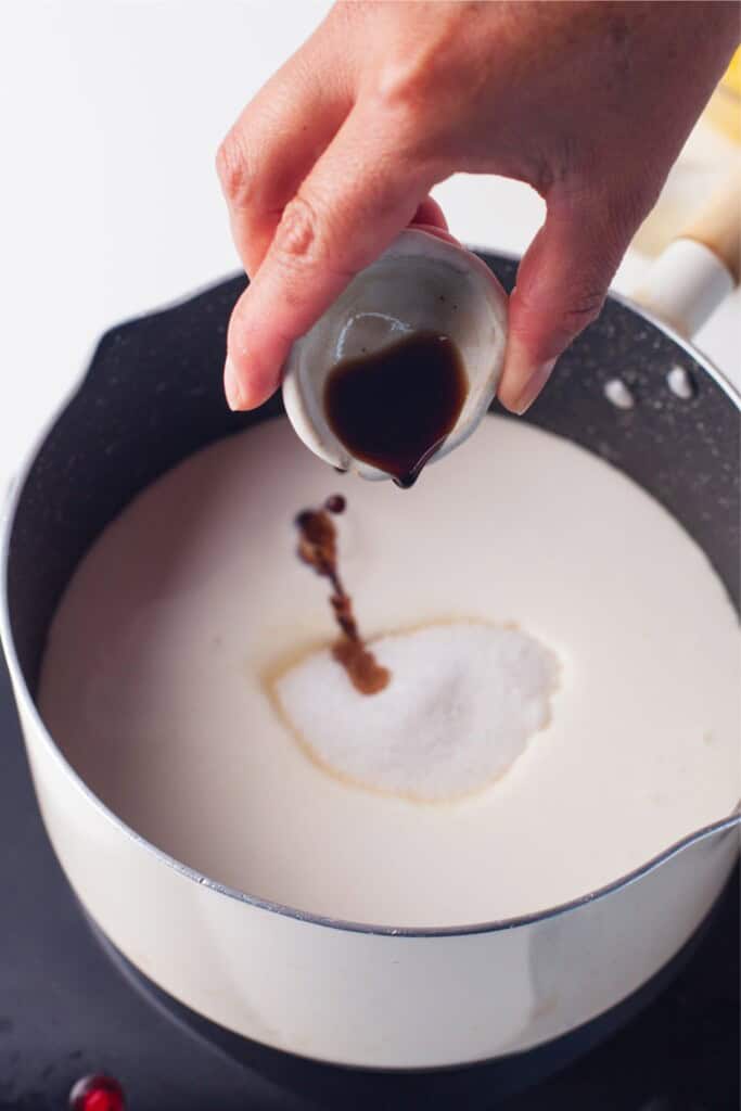 Adding vanilla extract to heavy cream and sugar in a saucepan for panna cotta