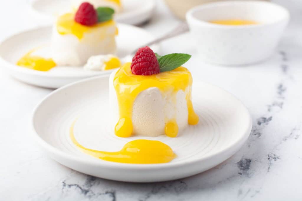 Panna cotta with mango sauce dripping down the sides, topped with a raspberry and fresh mint