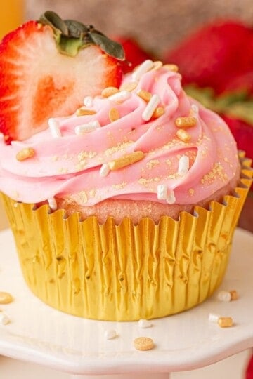 Pink champagne cupcake with strawberry slice in gold foil liner on cake stand