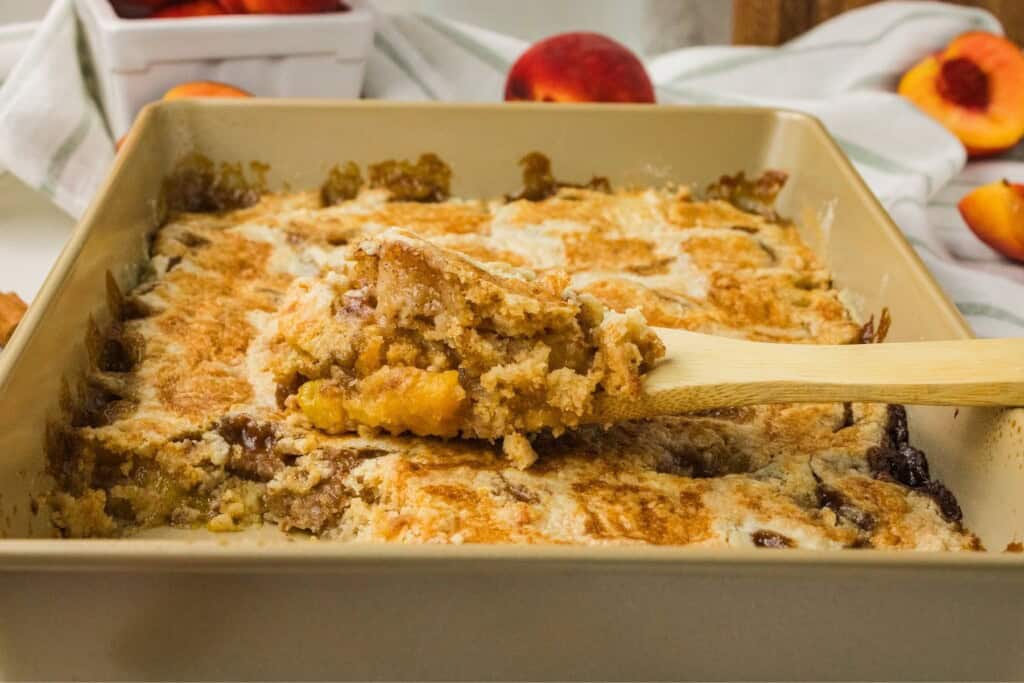 wooden spoon scooping peach dump cake showing peach layer