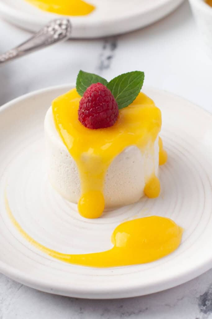 Vanilla panna cotta with mango sauce on a white plate, garnished with a raspberry and mint leaves