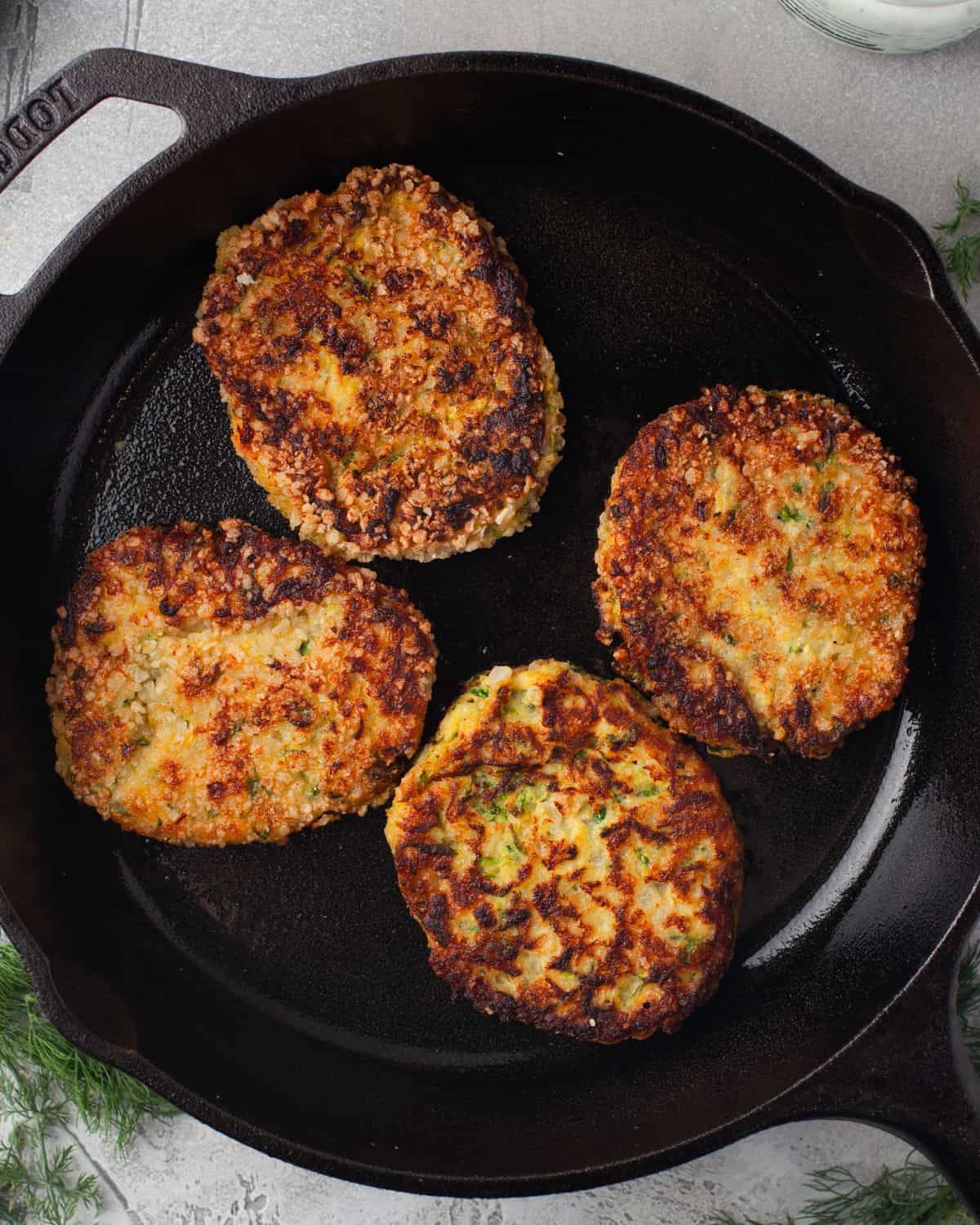 Zucchini patties with feta and tzatziki sauce in a skillet