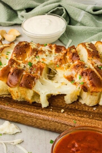 Air fryer Hawaiian roll garlic bread on a wooden board with melted mozzarella cheese pull and marinara and ranch dipping sauces