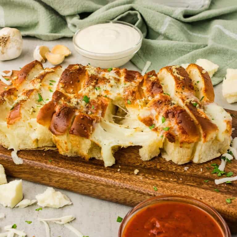 Air fryer Hawaiian roll garlic bread on a wooden board with melted mozzarella cheese pull and marinara and ranch dipping sauces