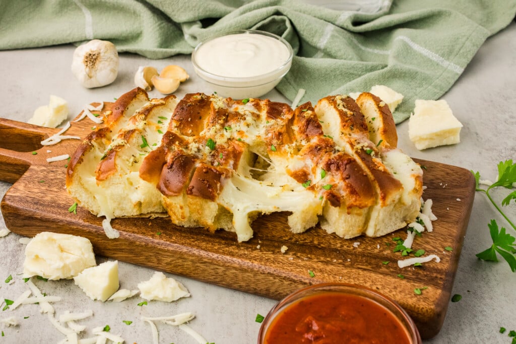 Air fryer Hawaiian roll garlic bread on a wooden board with melted mozzarella cheese pull and marinara and ranch dipping sauces 