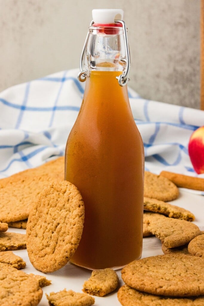 Bottle of fresh apple cider surrounded by brown butter apple cider snickerdoodles 