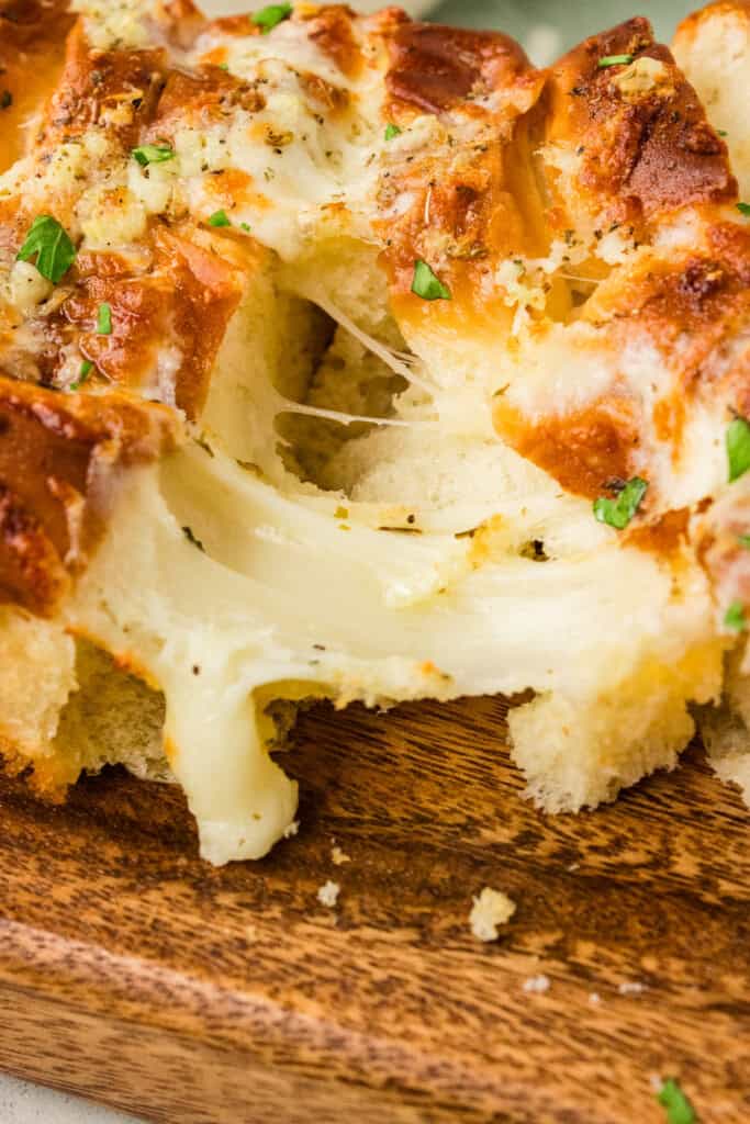Single cheesy garlic Hawaiian roll on a white plate with the pull-apart loaf behind 