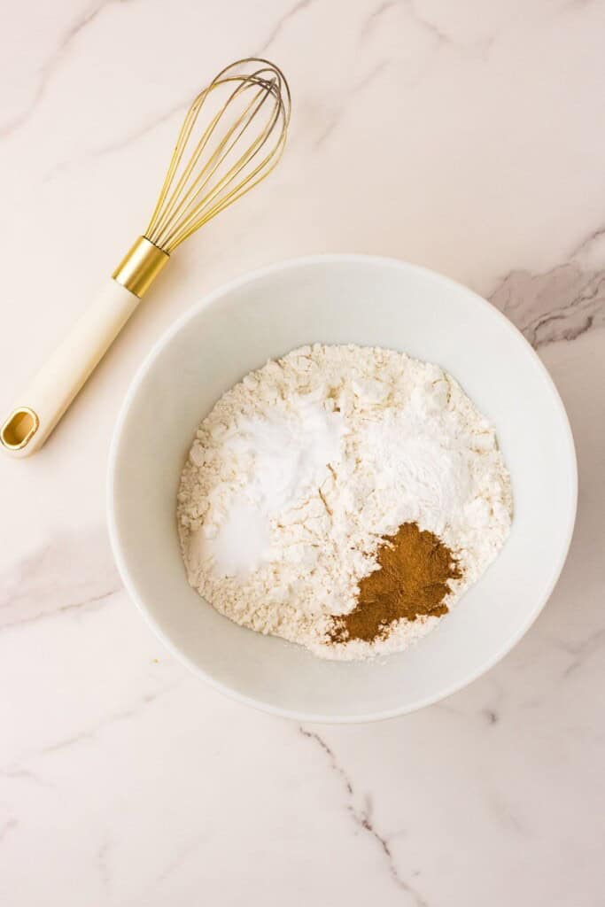 Flour, cream of tartar, baking soda, cinnamon and salt whisked together in a white bowl 