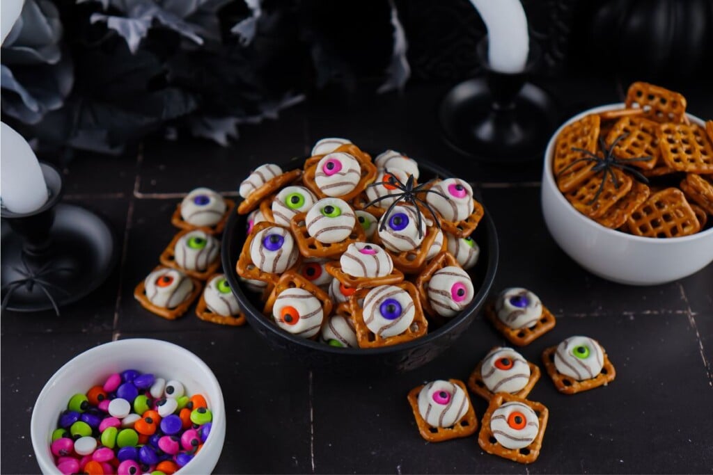 Halloween party table set with a bowl of eyeball pretzel bites, a bowl of pretzel snaps and a bowl of candy eyes
