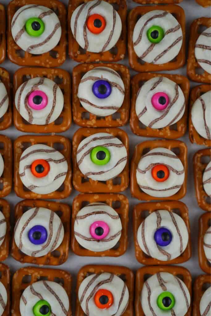 Close overhead grid of Halloween pretzel bites showing the chocolate rim that forms around each candy eye