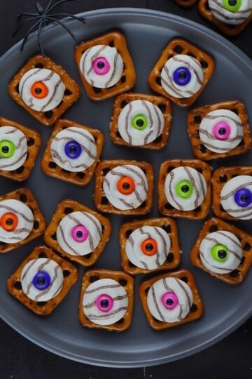 Overhead plate of eyeball pretzel bites with green, purple, pink and orange candy eyes