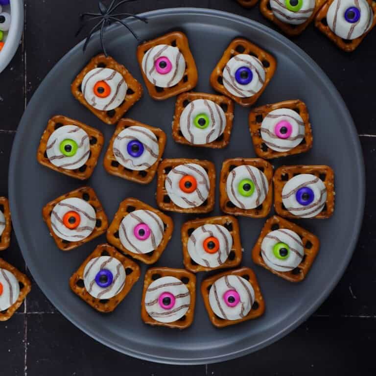 Overhead plate of eyeball pretzel bites with green, purple, pink and orange candy eyes