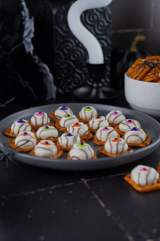 Plate of eyeball pretzel bites on a dark table with black Halloween decor behind
