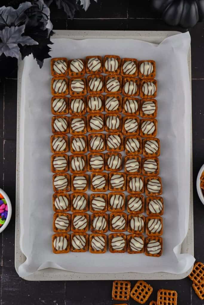 Unwrapped Hershey Hug onto a pretzel snap on a lined baking sheet