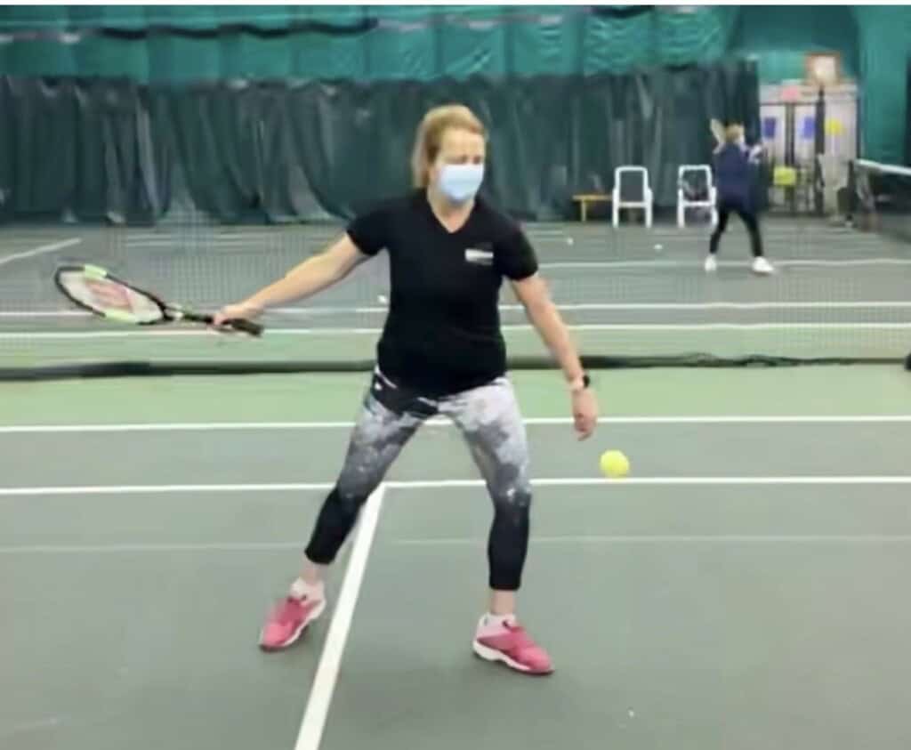 Angela on an indoor tennis court in 2020, wearing a face mask, getting ready to hit a forehand.