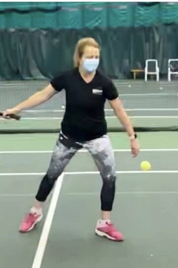 Angela on an indoor tennis court in 2020, wearing a face mask, getting ready to hit a forehand.
