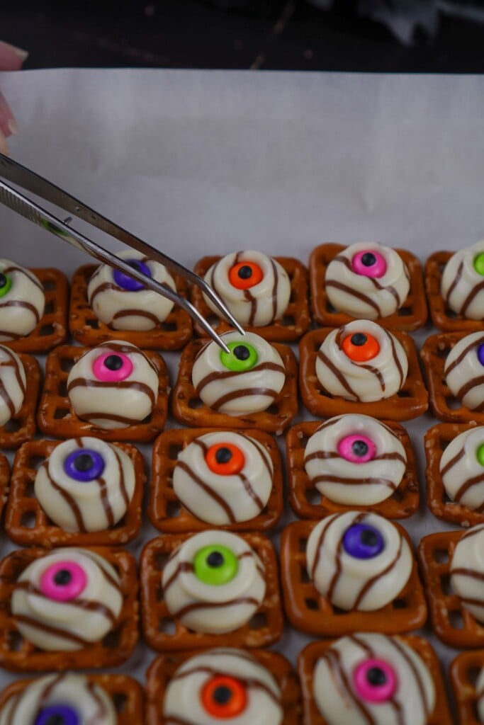 Baking tweezers pressing a green candy eye into the center of a warm Hershey Hug