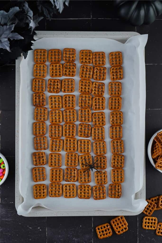 Pretzel snaps arranged in rows on a parchment lined baking sheet